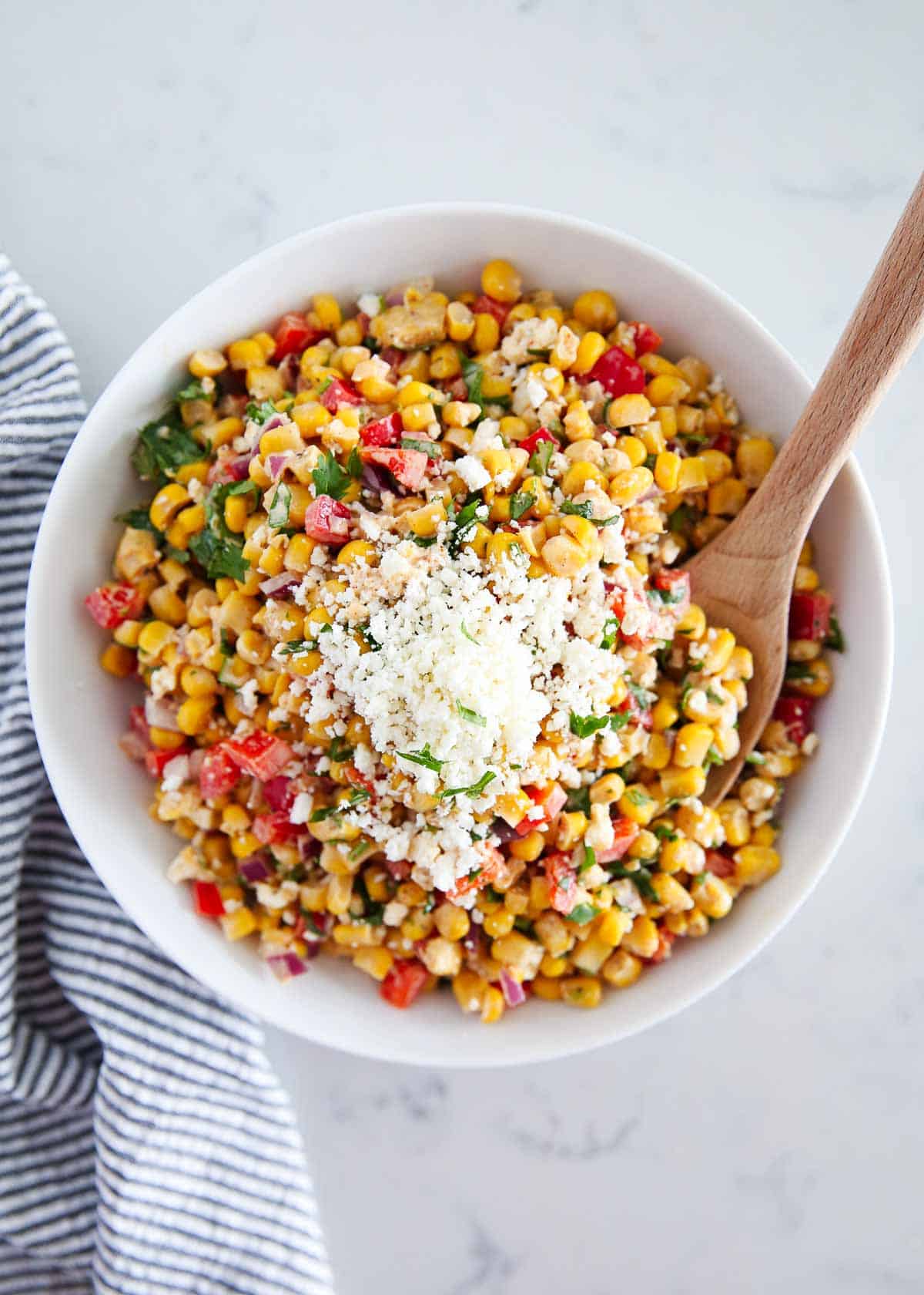 Mexican street corn salad in a white bowl with serving spoon.