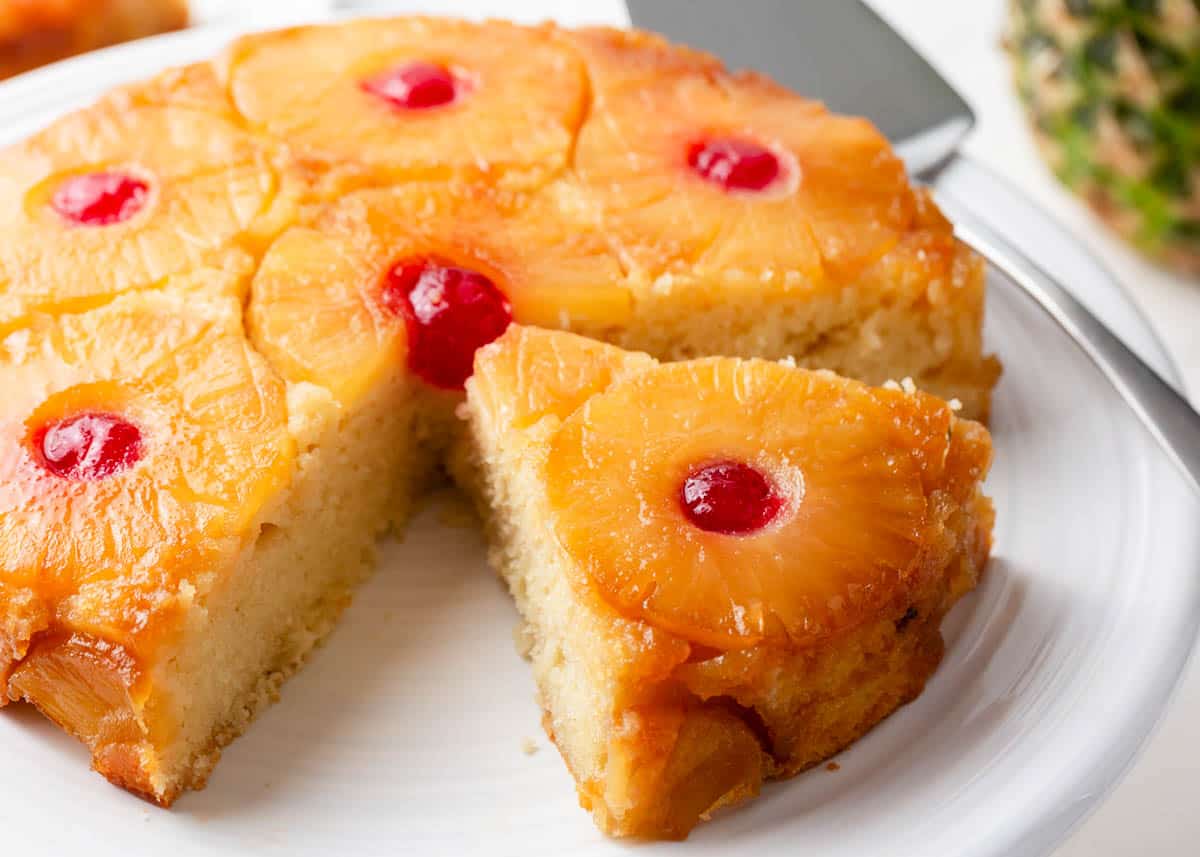 This easy pineapple upside down cake is made with a moist, buttery vanilla cake base adorned by a caramelized pineapple topping dotted with maraschino cherries. It's a classic recipe with melt-in-your-mouth results. Pineapple upside down cake on white plate.