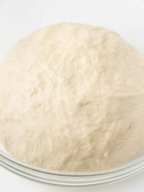 Homemade pizza dough with active dry yeast in a clear bowl.