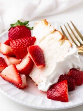 A slice of angel food cake with sweetened strawberries and whipped topping.
