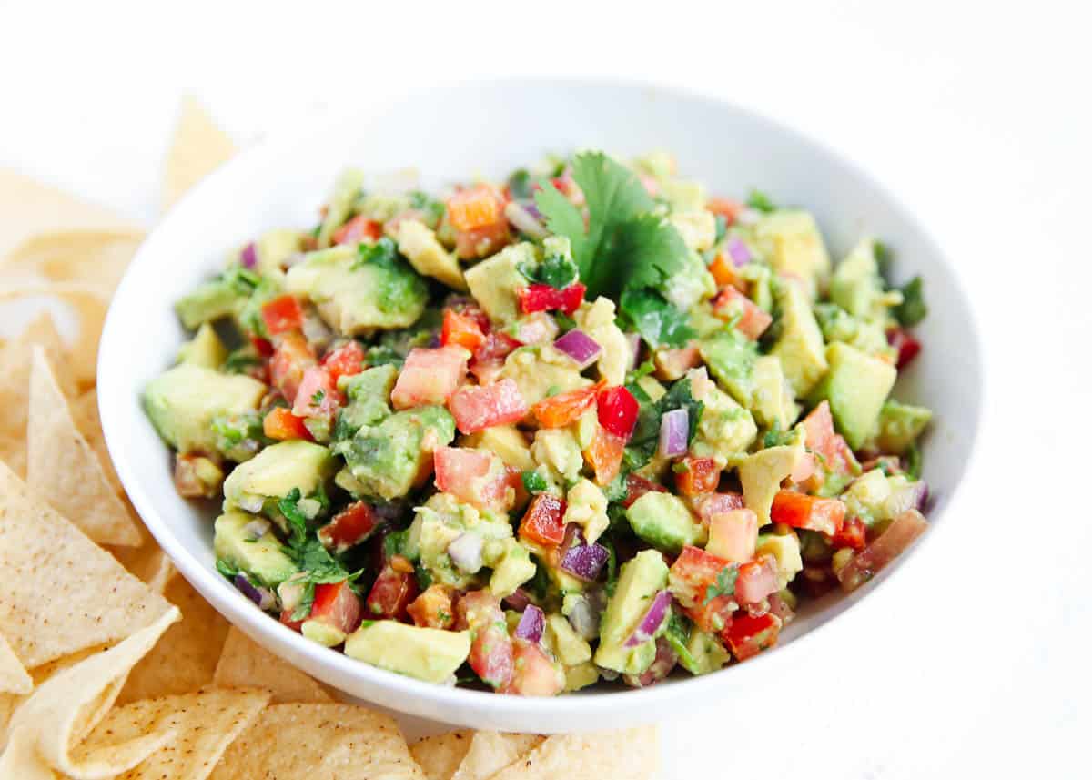 Avocado salsa in a white bowl with chips on the side.