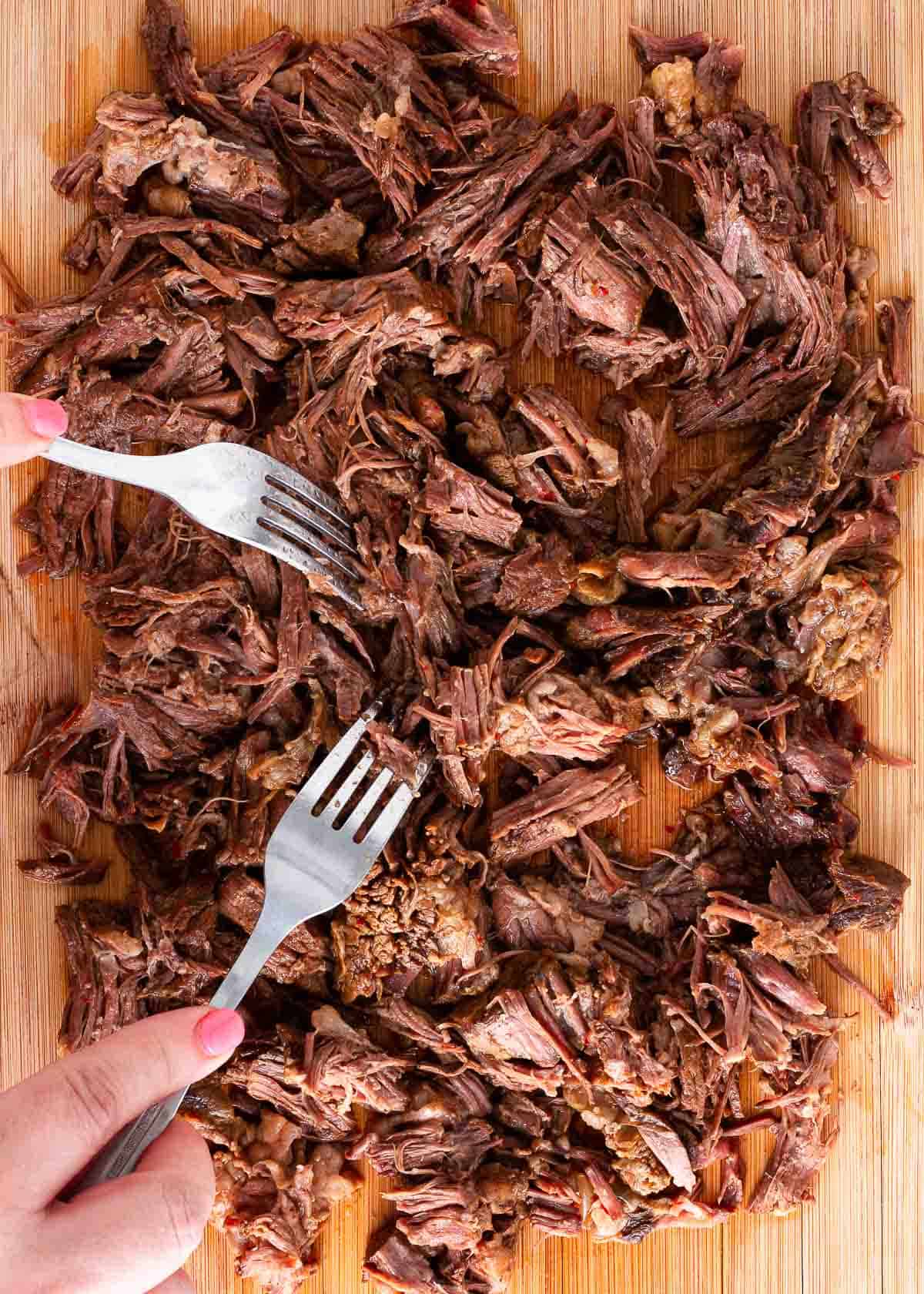 Shredding beef birria onto a cutting board.