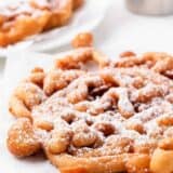 Funnel cake on a white plate with powdered sugar.