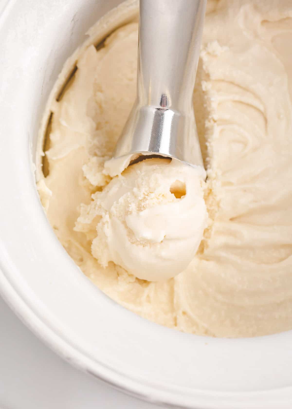 Vanilla ice cream with a ice cream scooper in the middle of the bowl. 