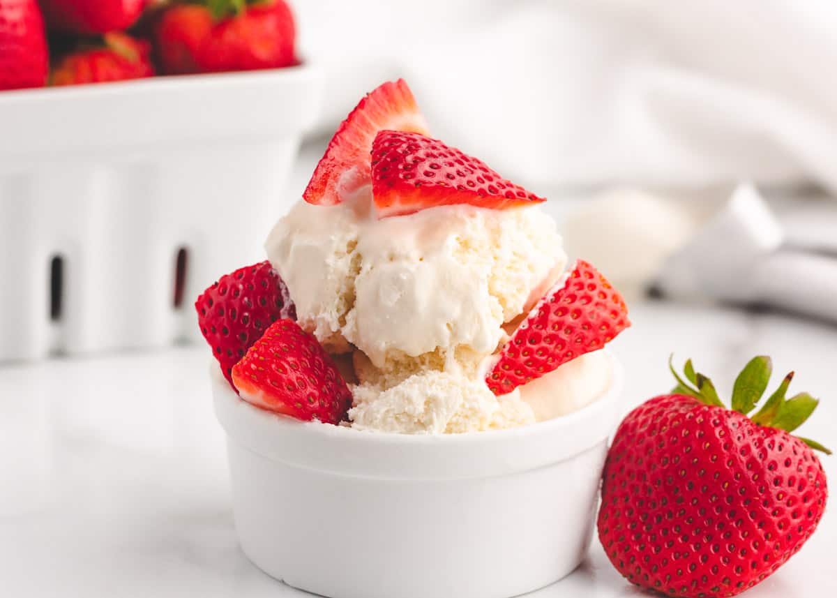 Vanilla ice cream in a bowl with strawberries over top. 