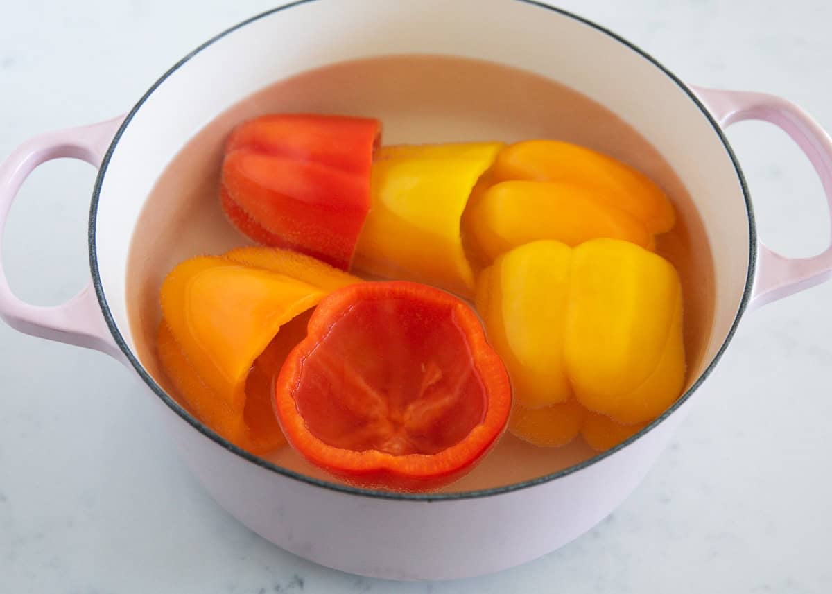 Whole bell peppers with tops removed boiling in a pot of water before stuffing.
