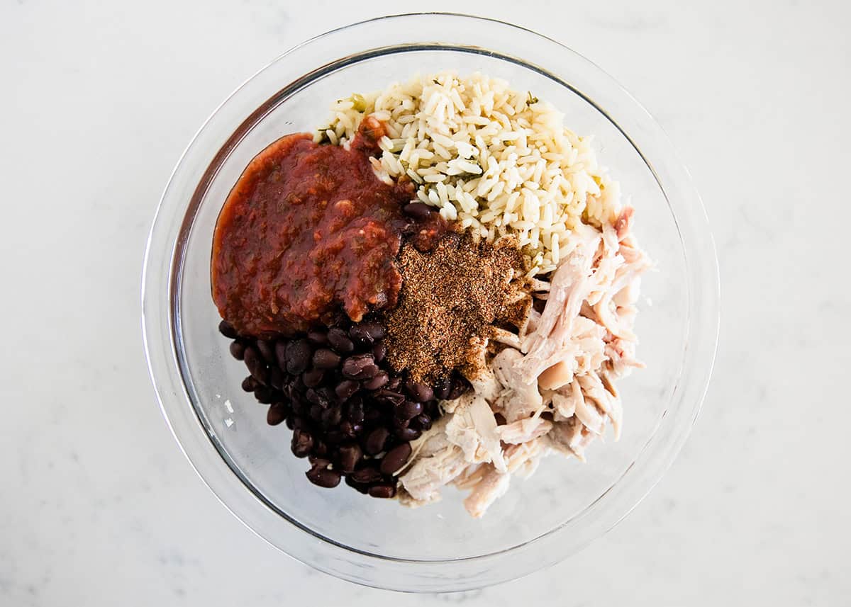 Shredded chicken, rice, black beans, salsa and taco seasoning in a glass bowl.