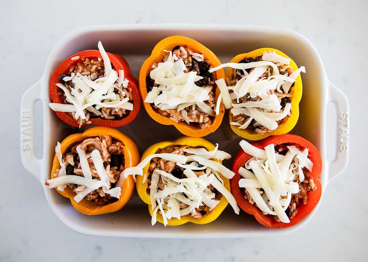 Chicken stuffed peppers topped with shredded cheese in a white baking dish, ready to bake.