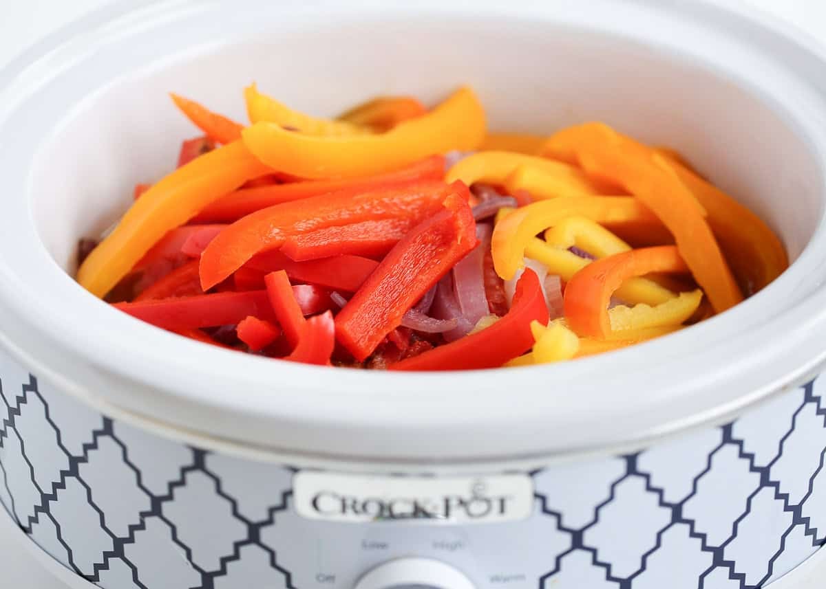 Sliced red, orange, and yellow bell peppers added on top in a crockpot.