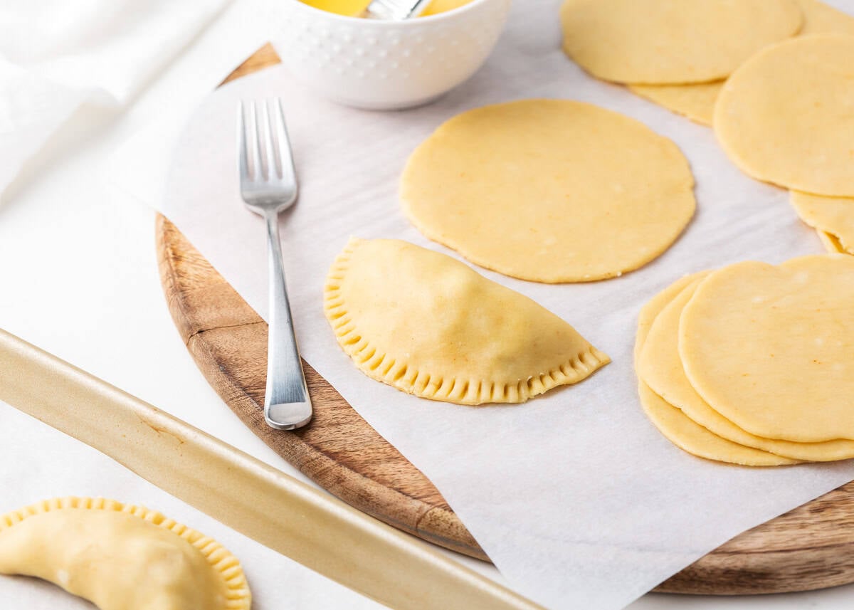 Folded and fork-crimped empanada next to rolled dough discs ready to fill.