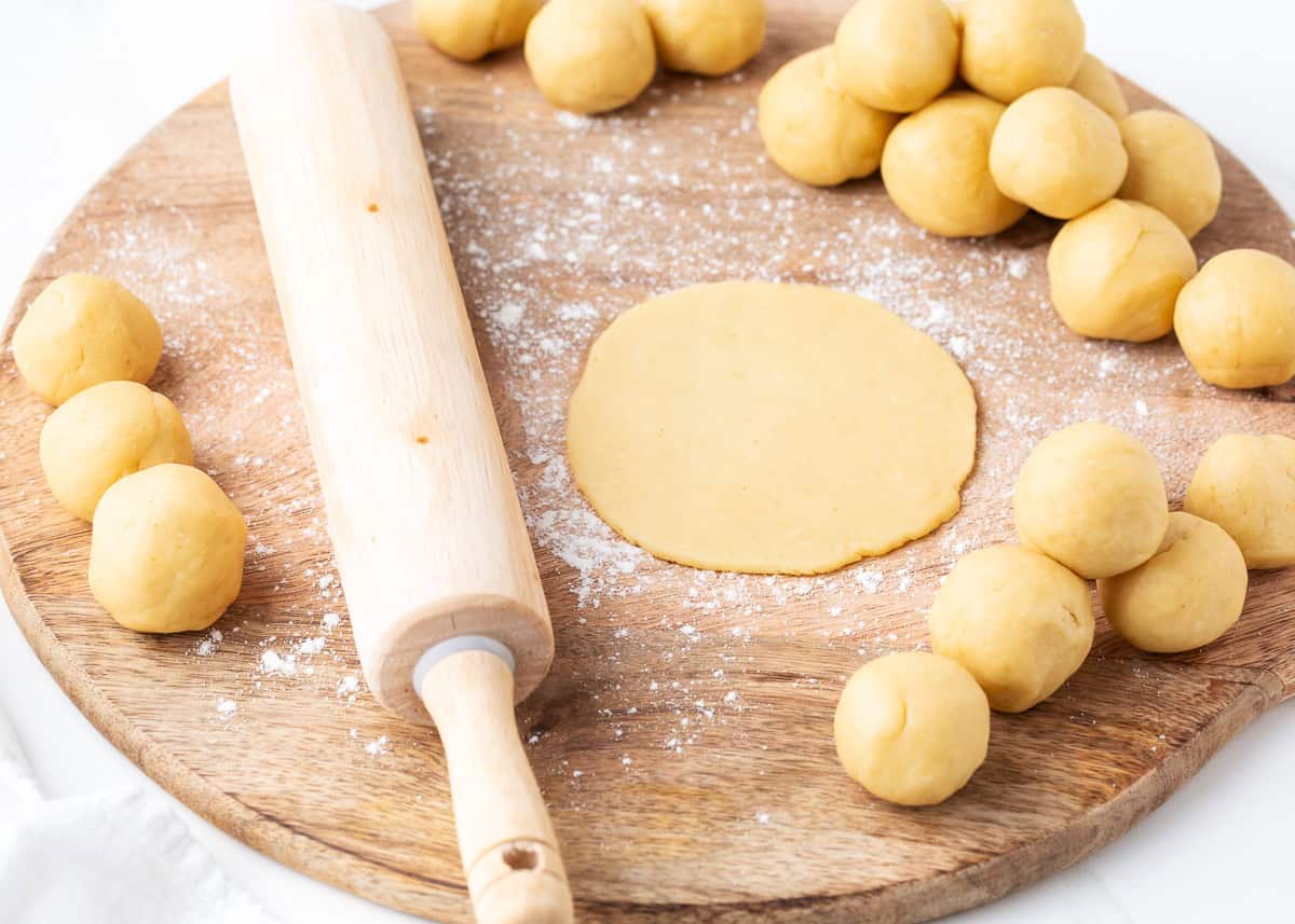 Rolling empanada dough balls into flat discs with a rolling pin on a floured board.