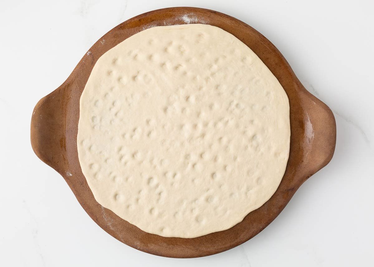 Unbaked pizza dough shaped into a 12-inch round on a pizza stone, ready for toppings.