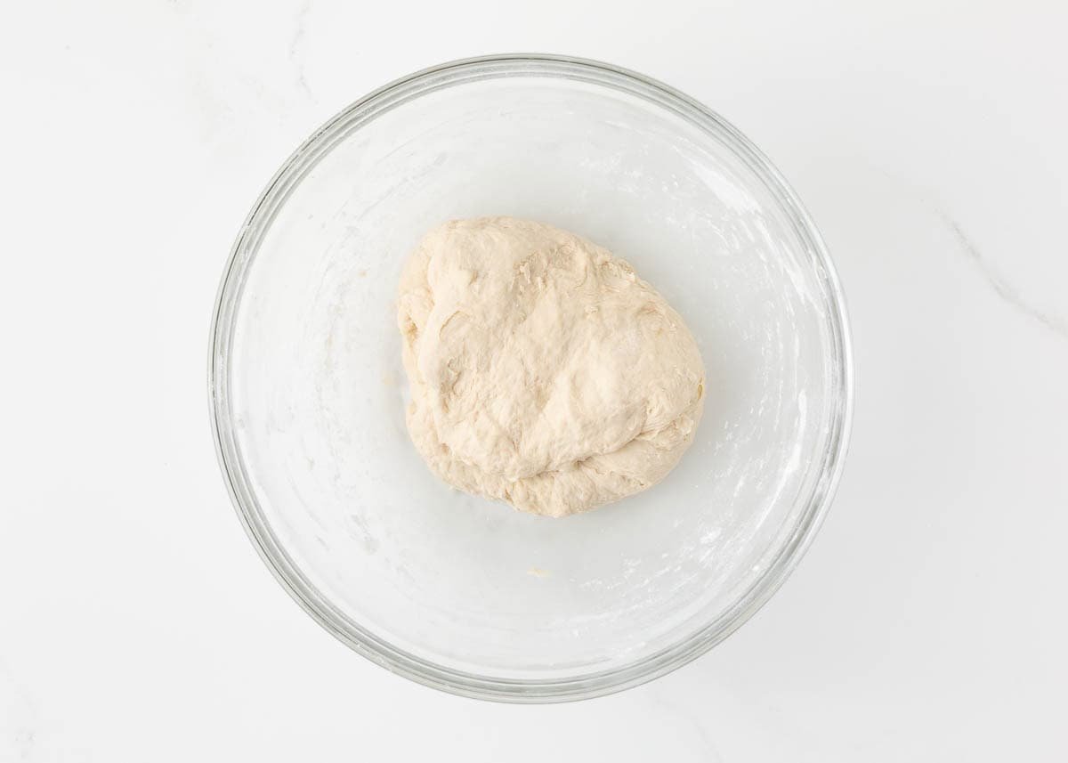 Smooth ball of pizza dough after kneading, resting in a lightly oiled bowl.
