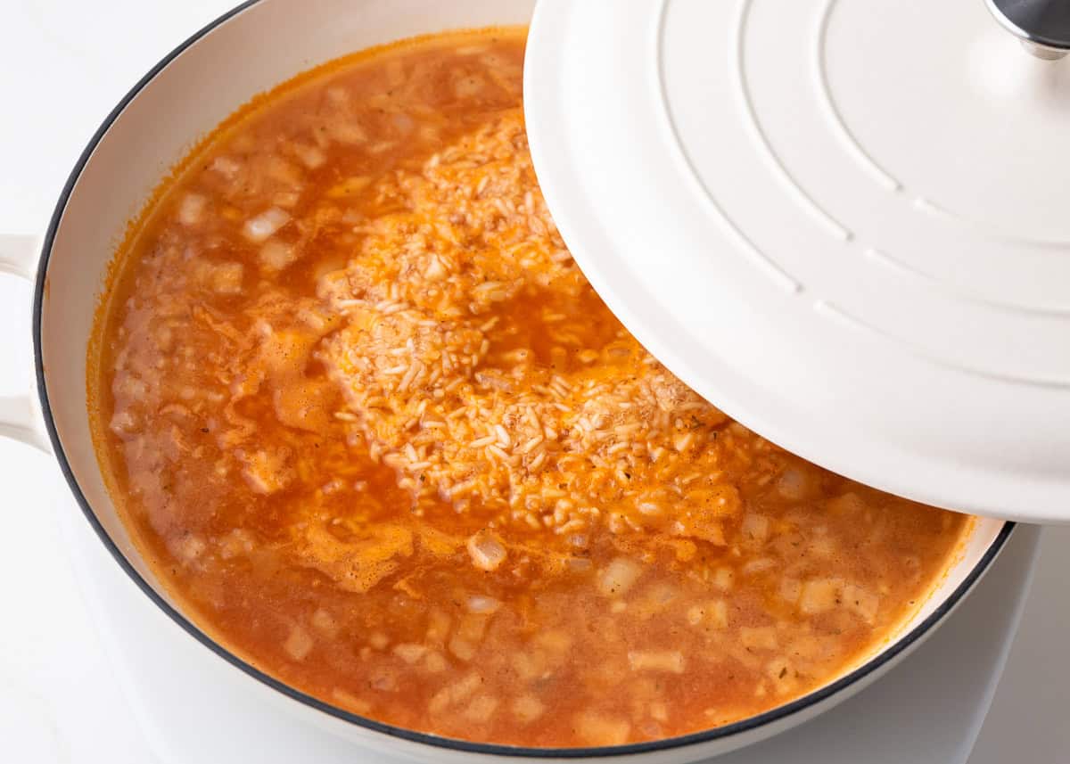 Simmering rice with tomato sauce and spicesin a skillet.