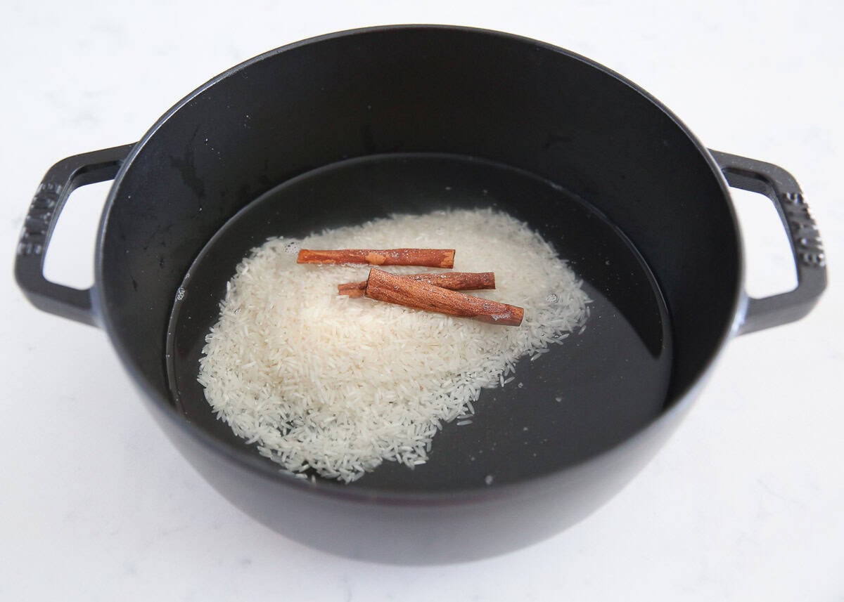Rice and cinnamon sticks added to water in a large black pot.