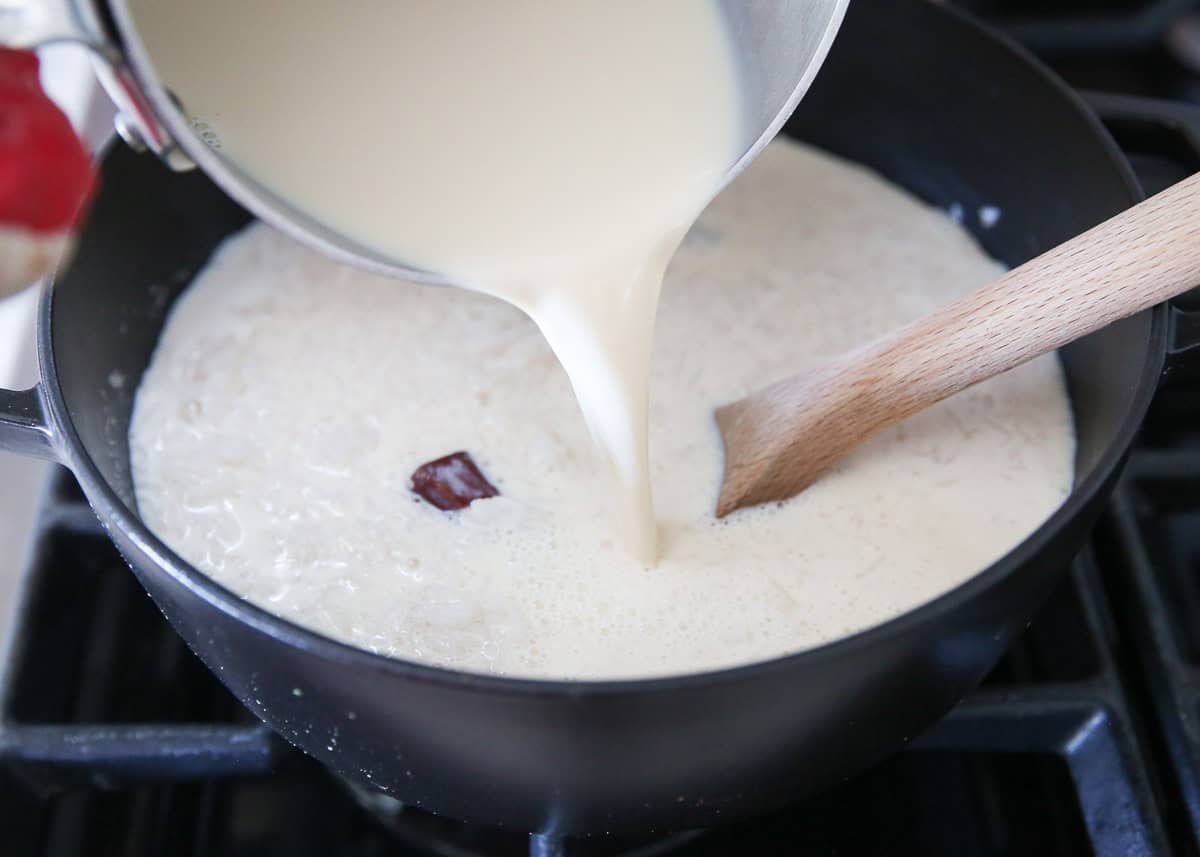 Pouring warm milk mixture into cooked rice to make arroz con leche.