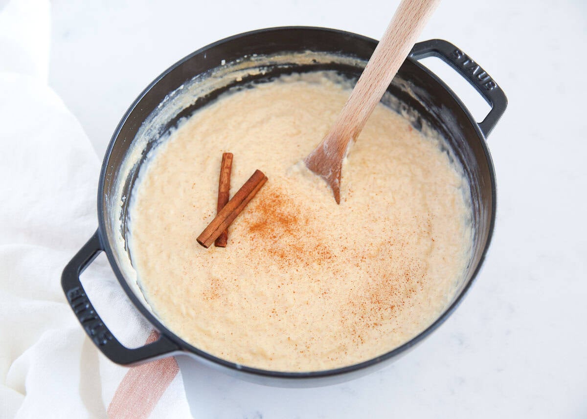 Finished Mexican rice pudding in a black pot topped with cinnamon sticks and a dusting of ground cinnamon.