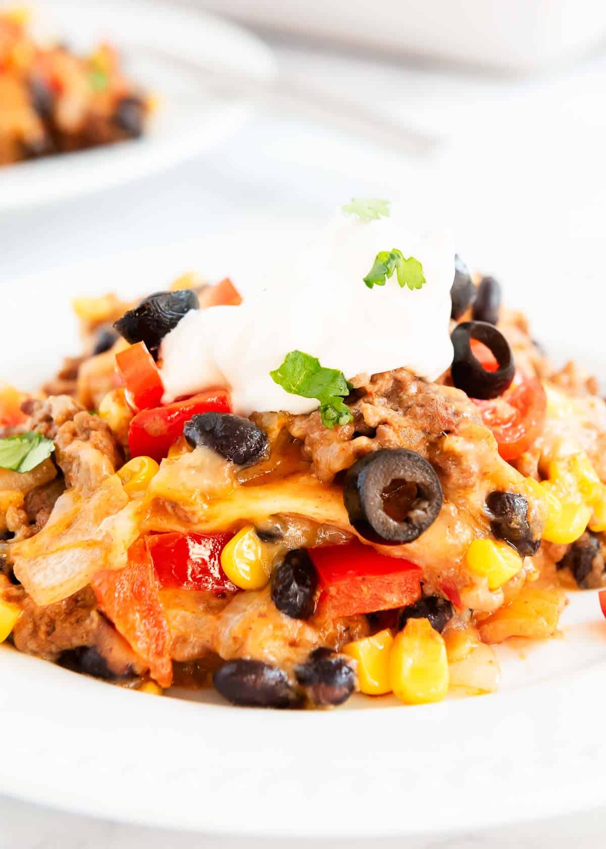 Mexican lasagna on a white plate with all the toppings. 