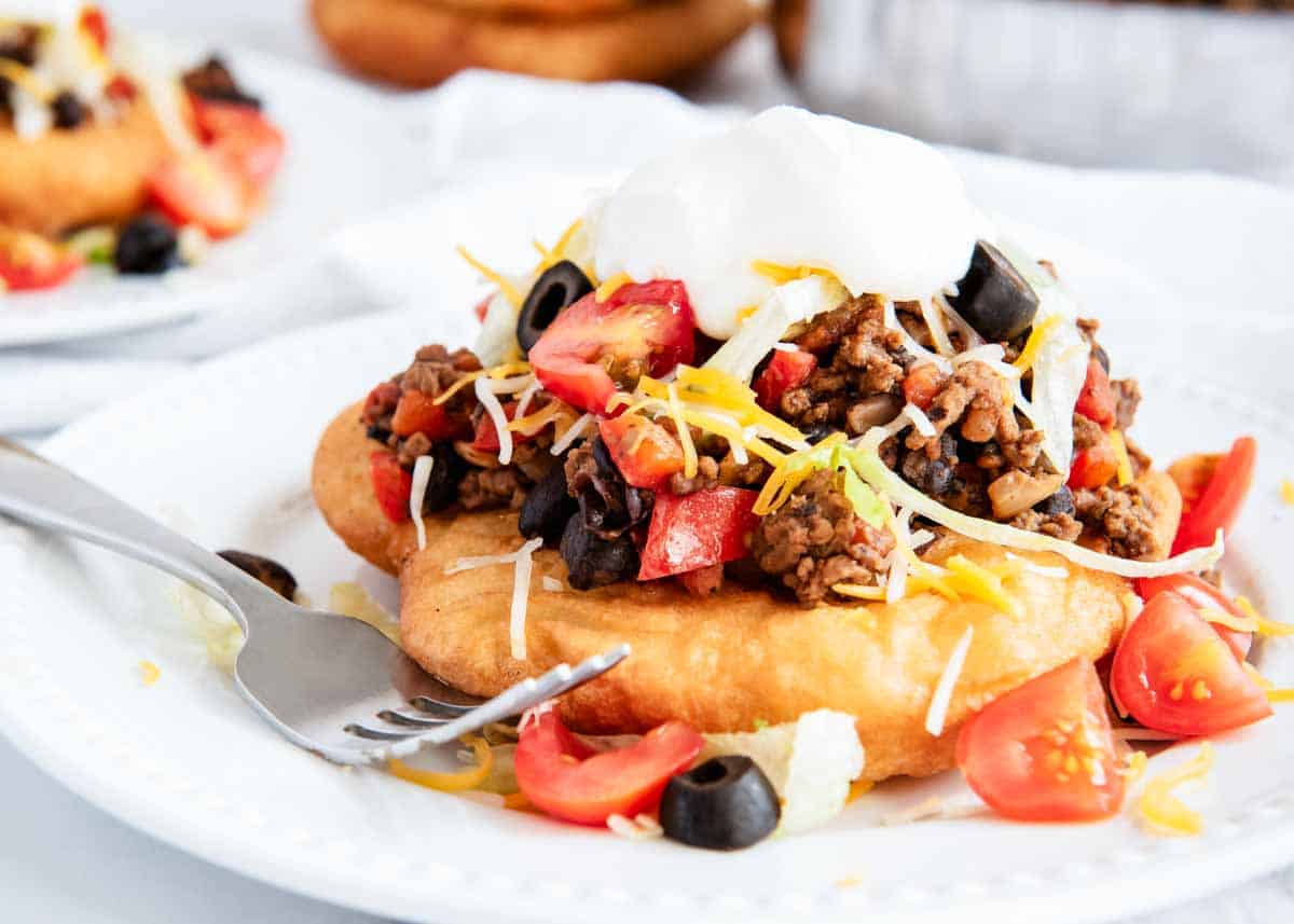 Navajo tacos filled with ingredients on a white plate with a fork. 