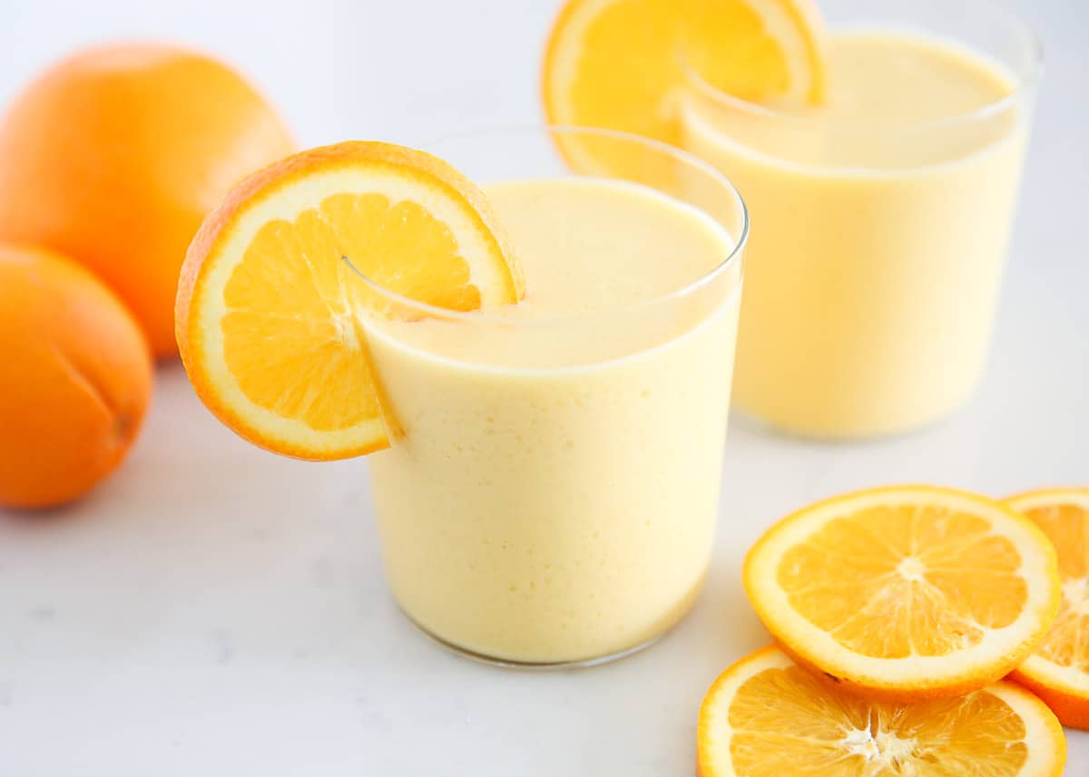 Orange Julius in a glass cup with oranges.