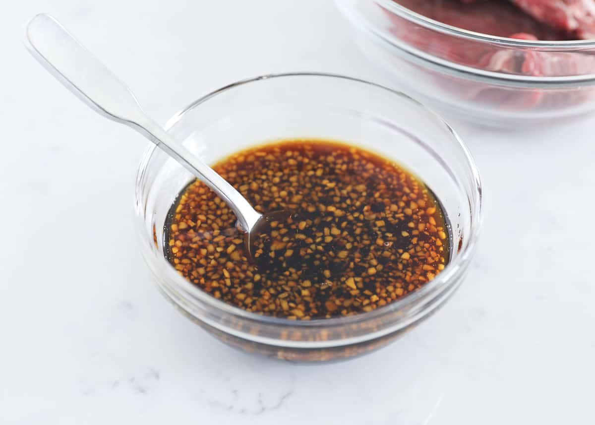 Steak marinade in a glass bowl with a spoon in it. 