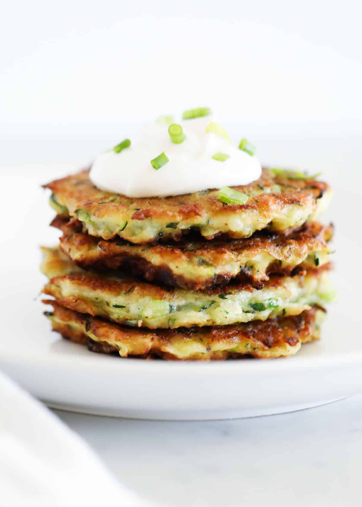 A stack of zucchini fritters on a plate with a dollop of whipped cream.