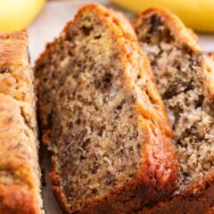 Sliced banana nut bread showing moist texture and yellow bananas in background.