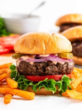 Juicy homemade hamburger patty on a toasted bun with toppings and fries served on the side.