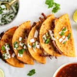 Five assembled birria tacos on parchment paper on the counter.