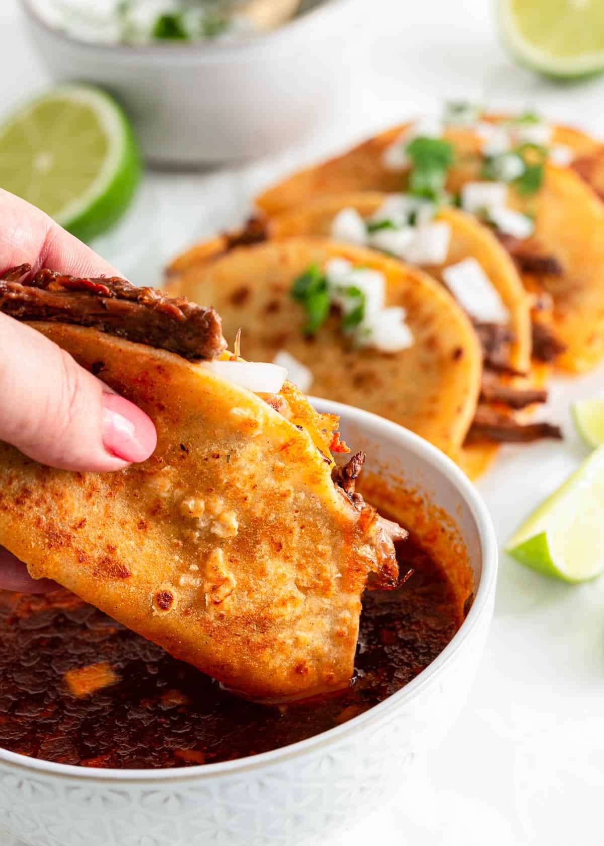 Dipping a birria taco in broth in a bowl.