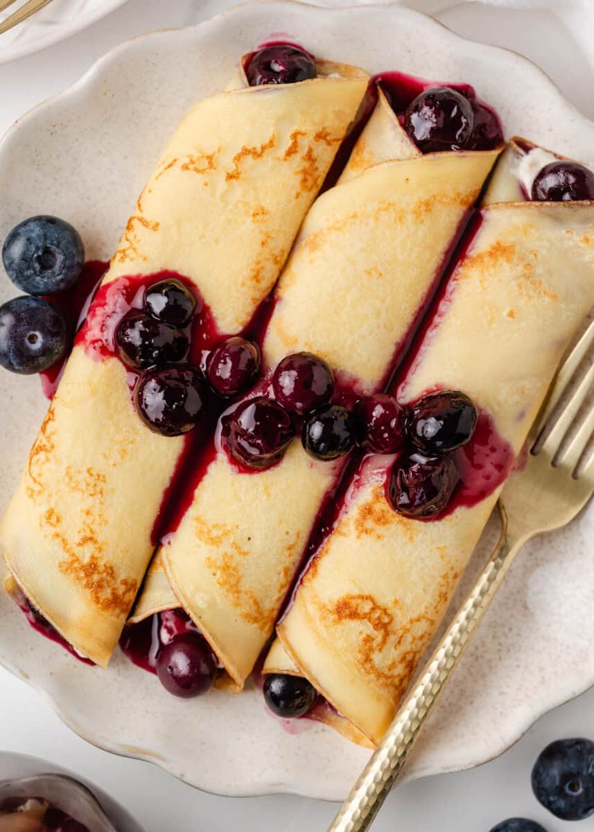 Close-up of rolled blueberry crepes filled with cream and fresh blueberries, drizzled with blueberry sauce.