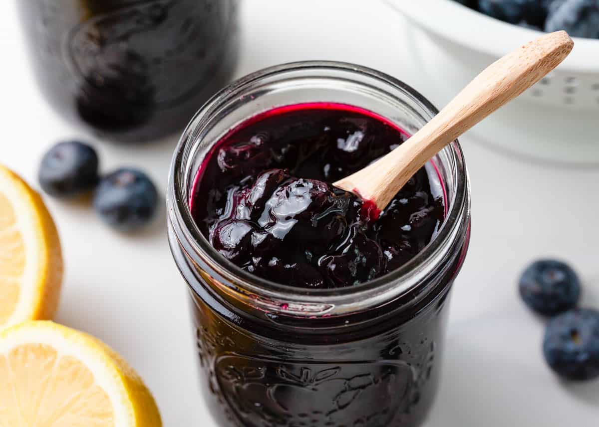 Blueberry jam in small glass jar with wood spoon.