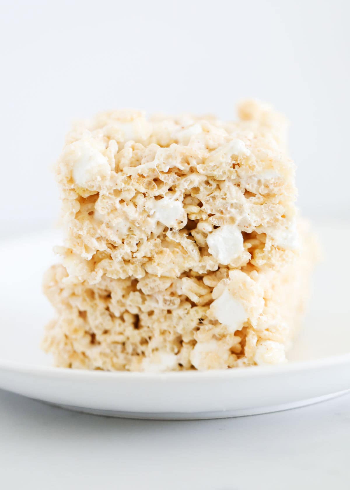 These brown butter rice krispie treats are like the classic but with a small updated twist! Brown butter gives the sticky, gooey treats a delicious nuttiness that is irresistible. A stack of brown butter rice krispie treats on a white plate.