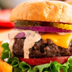 Juicy grilled cheeseburger stacked with lettuce, tomato, red onion, and pickles on a toasted brioche bun.