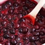 A close up of cherry pie filling in a pot with a wooden spoon.