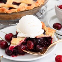 Slice of cherry pie with vanilla ice cream on a white plate.