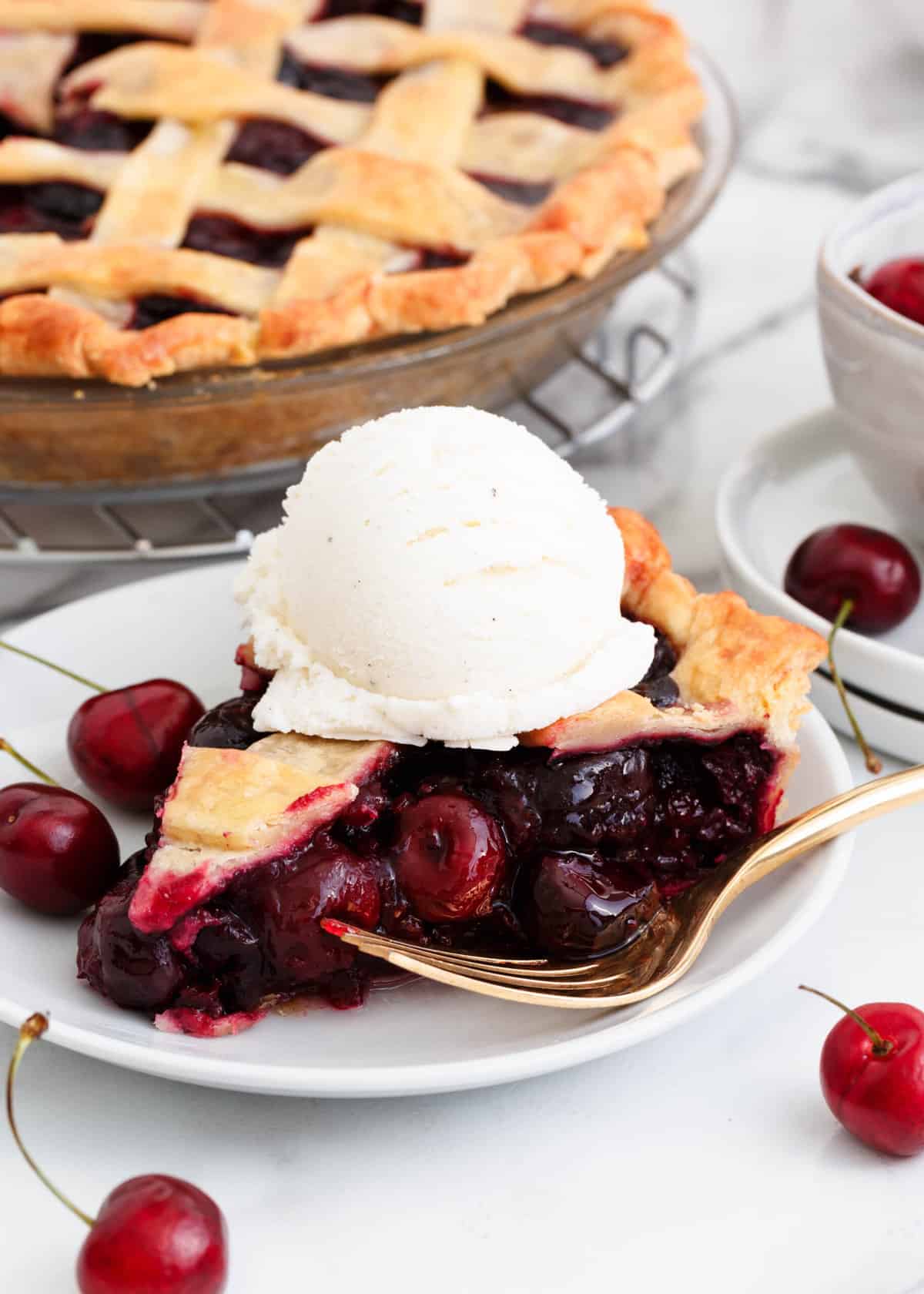 Slice of cherry pie with vanilla ice cream on a white plate.