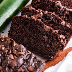 Sliced double chocolate zucchini bread on cutting board with fresh zucchini to the side.