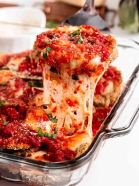 Pulling eggplant parmesan out of baking dish.