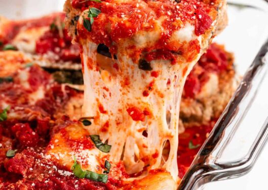 Pulling eggplant parmesan out of baking dish.