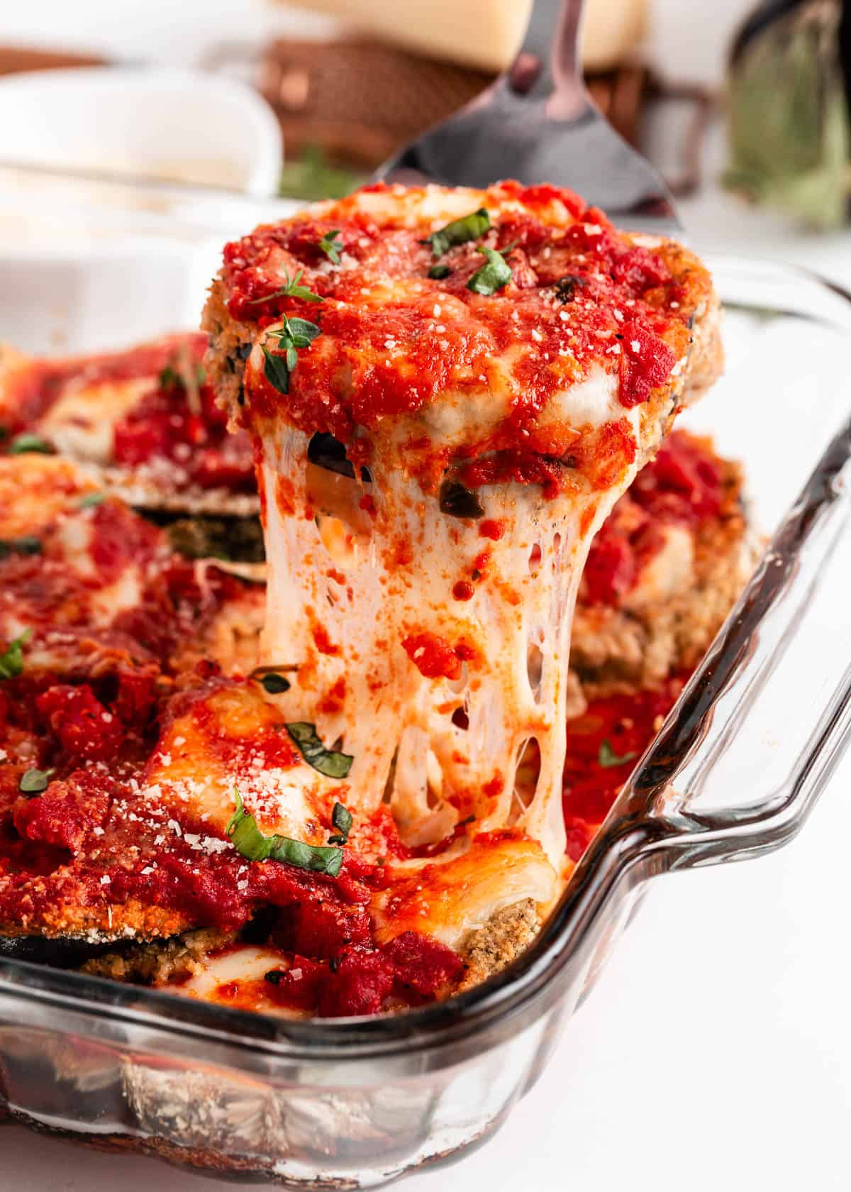 Pulling eggplant parmesan out of baking dish.