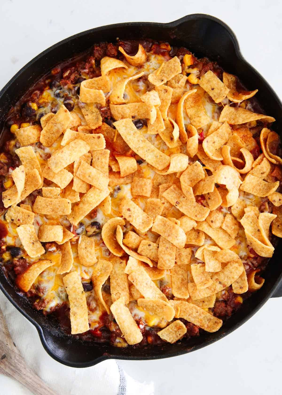This Frito pie is made with a taco seasoned ground beef base with beans and corn then baked with plenty of cheese and crunchy Fritos. It's a family friendly meal everyone loves! Frito pie in a skillet.