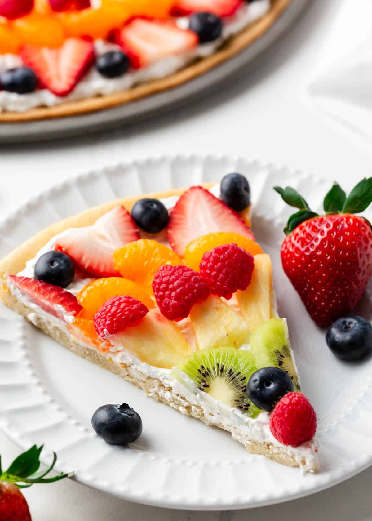 A slice of fruit pizza on a white plate.