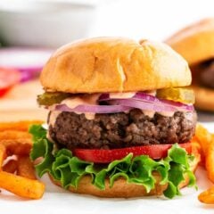 Grilled hamburger patty on a toasted bun with cheese, lettuce, onion, tomato and burger sauce.