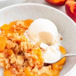 Peach cobbler and ice cream in a bowl with spoon.