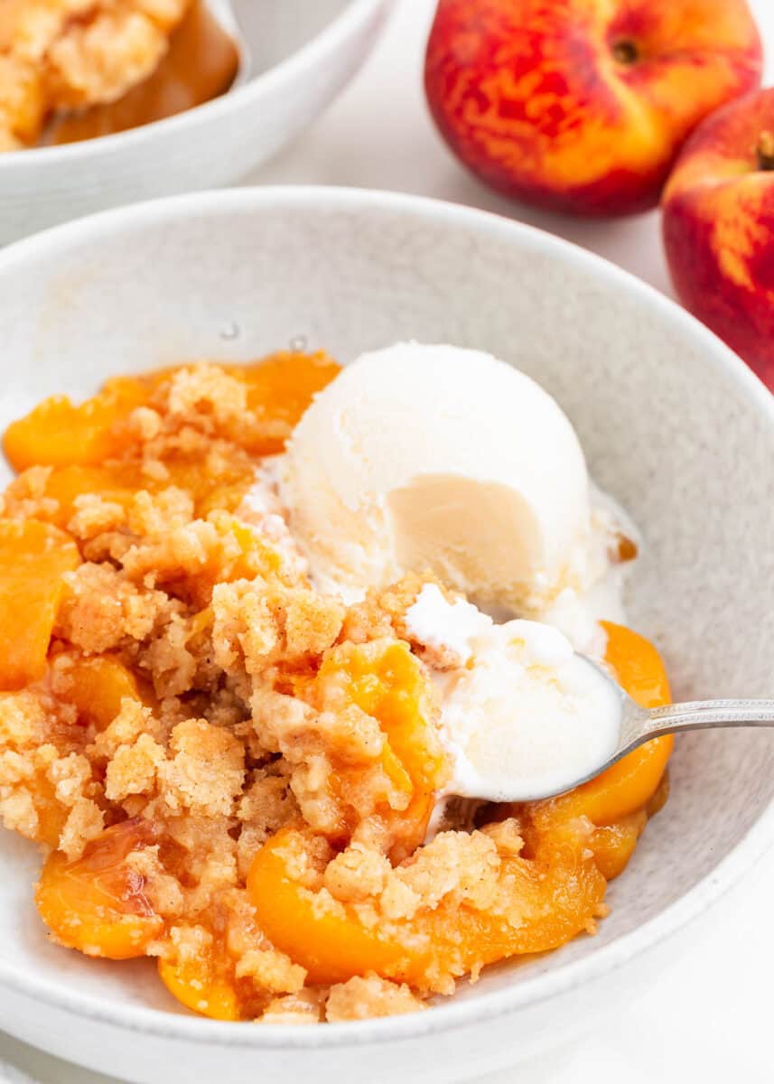 Peach cobbler and ice cream in a bowl with spoon.