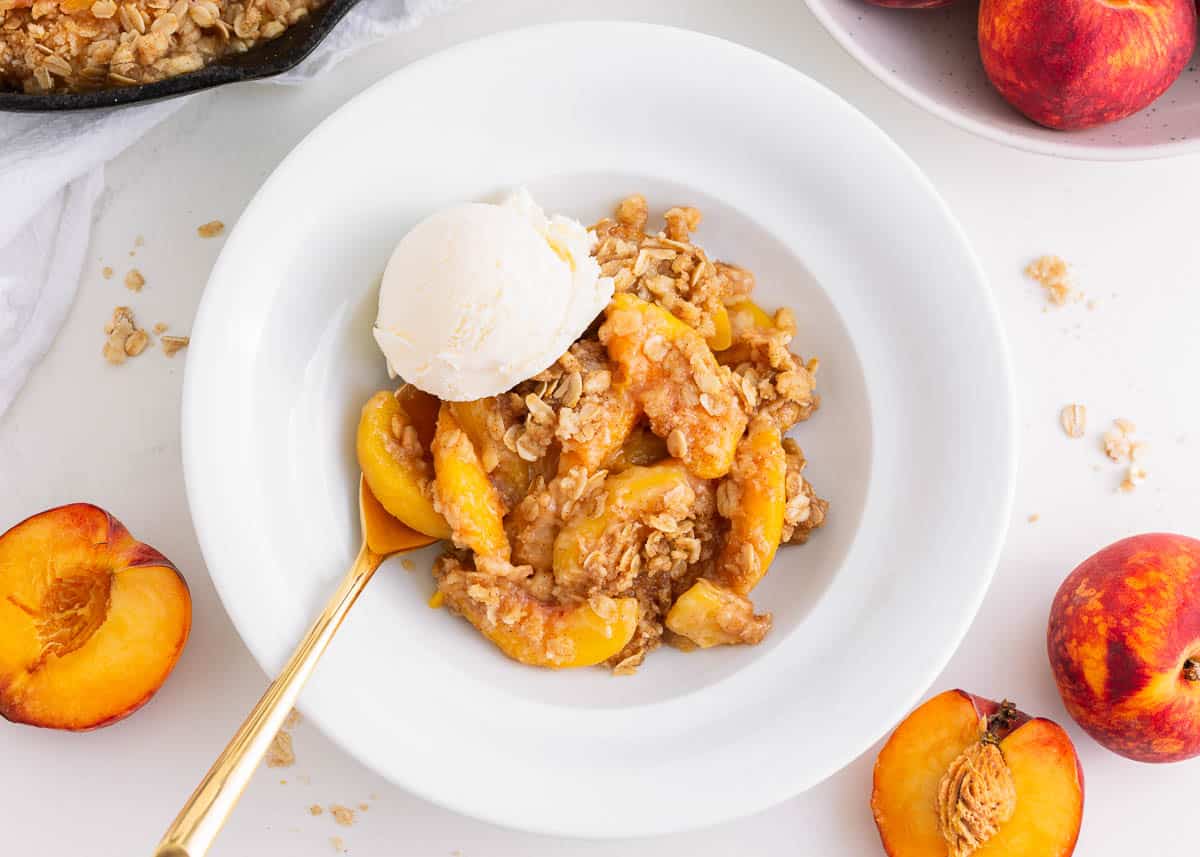 Peach crisp in a white bowl with ice cream.