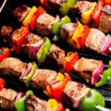 Steak kabobs cooking on a grill.
