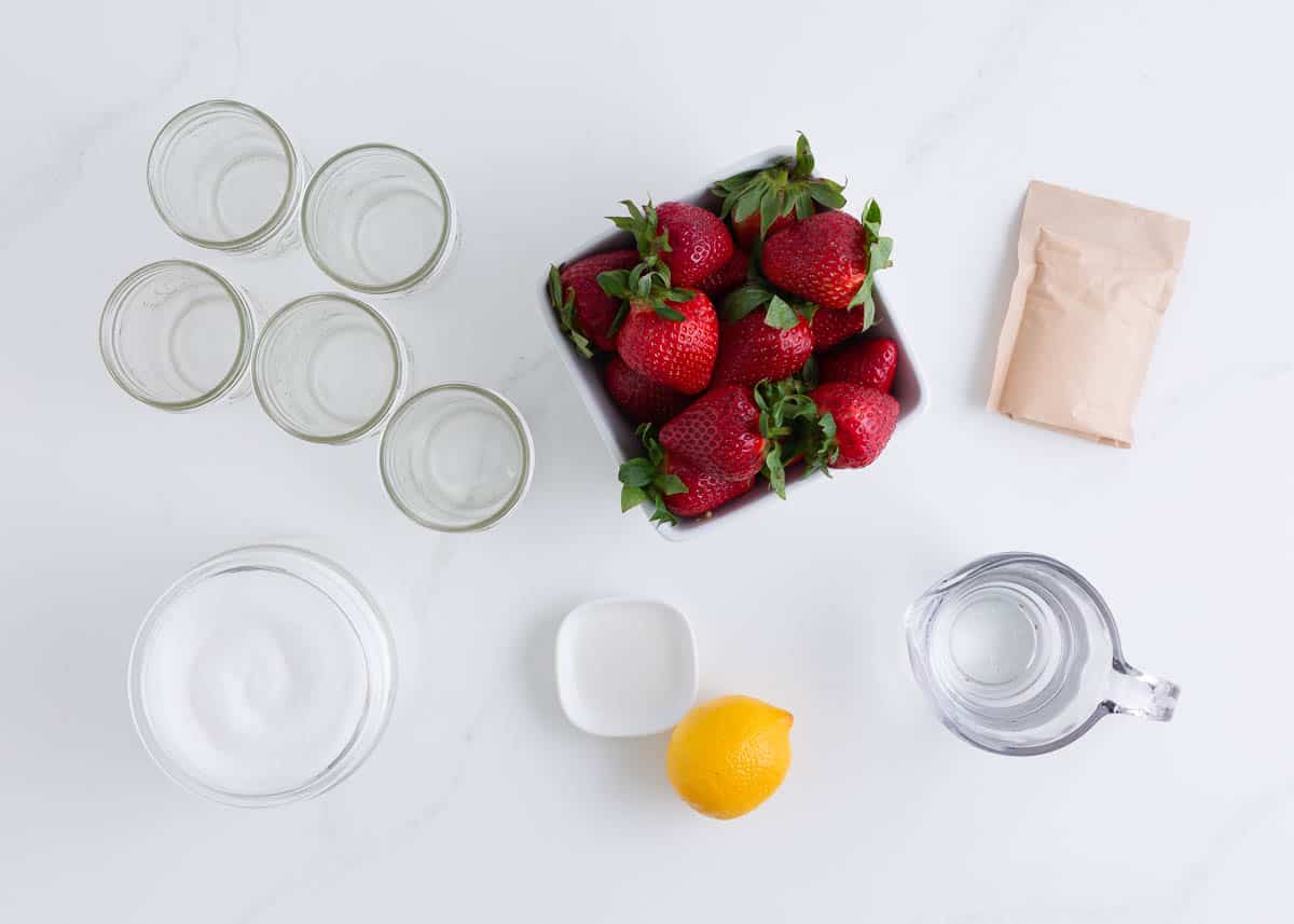 Strawberry jam ingredients including strawberries, lemon, sugar, pectin and water. 