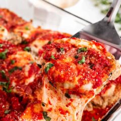 Slice of baked eggplant Parmesan being lifted from a casserole dish with layers of breaded eggplant, marinara sauce and melted mozzarella.